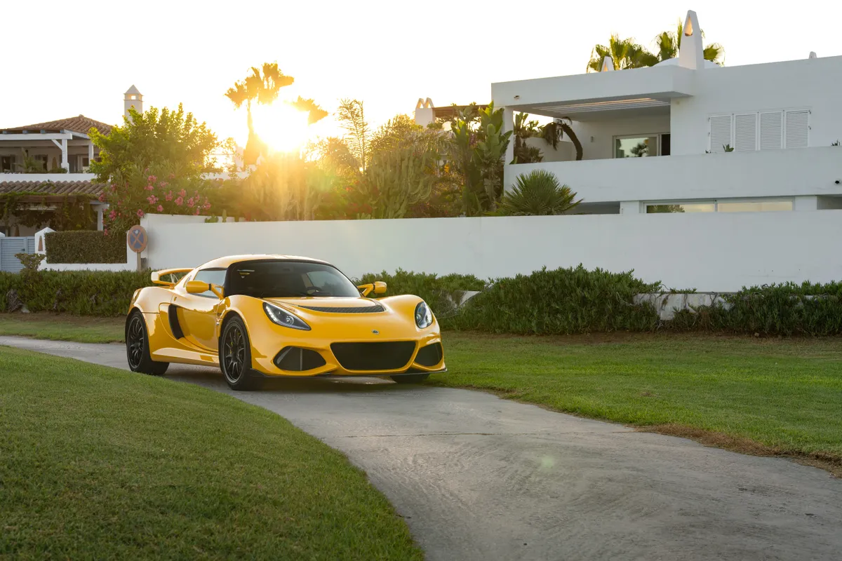 The Exige on a driveway with the sun breaking over the wall behind it