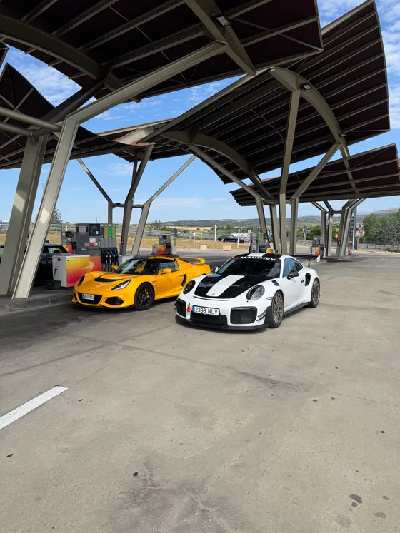The Exige parked under a canopy next to a Porsche GT2 RS