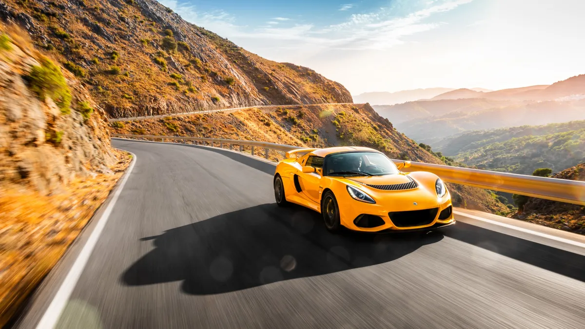 The yellow Exige at speed on a mountain pass, the road blurred beneath it